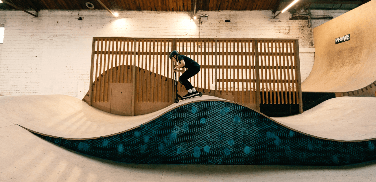 Boy riding a stunt scooter on a skate park ramp, practicing easy scooter tricks.