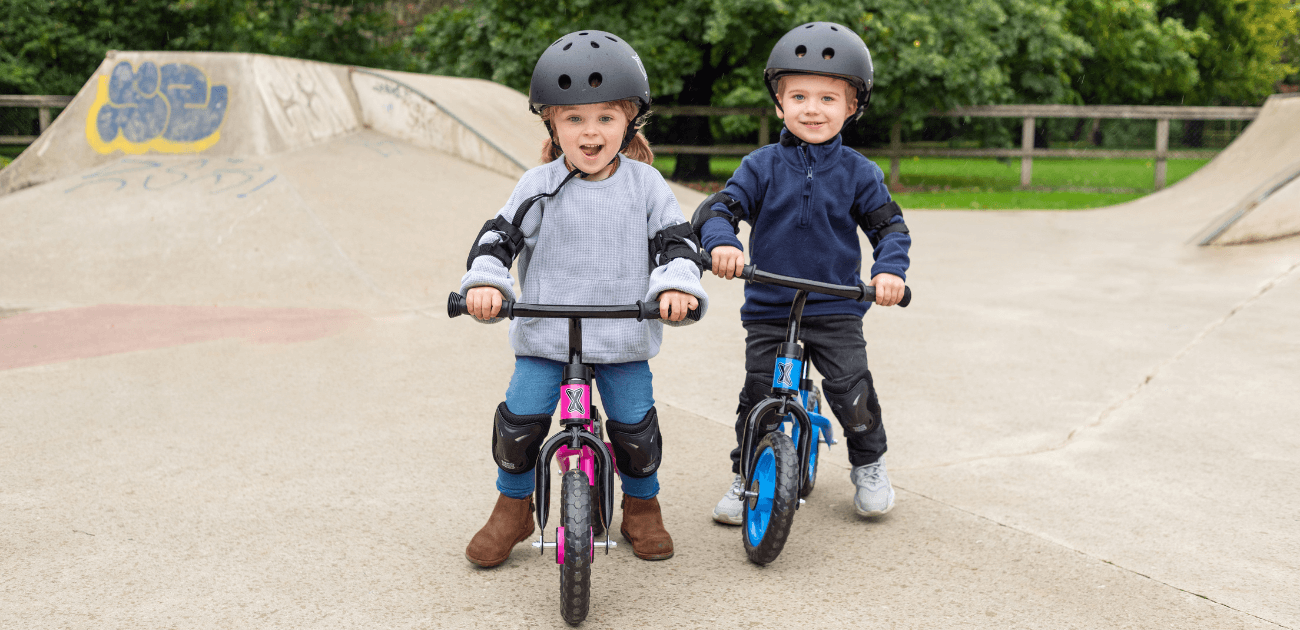 Two toddlers riding balance bikes in a park, showing the benefits of learning to ride early.