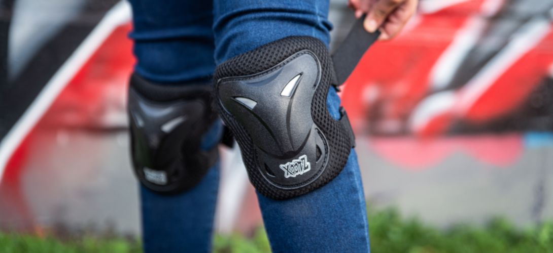 An image of a pair of black knee pads being worn over some jeans