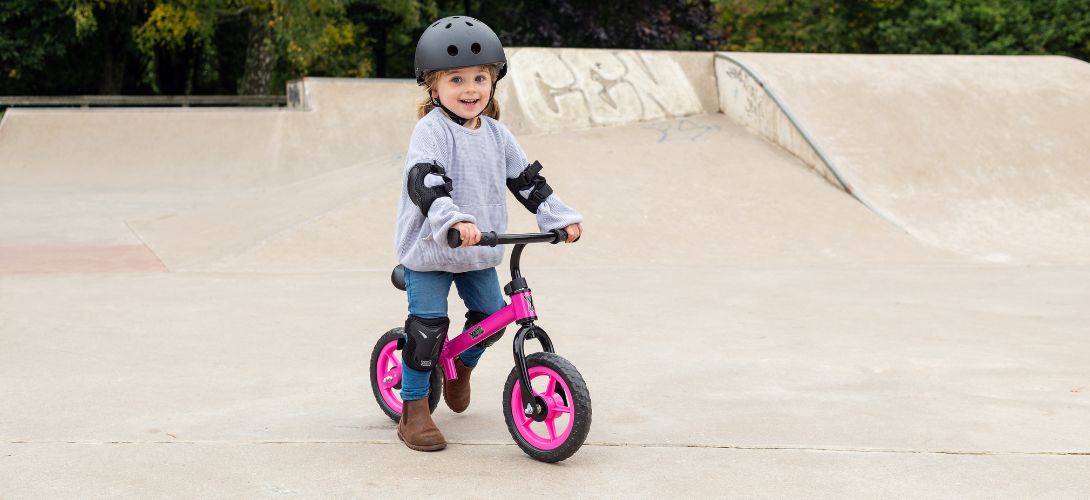 A photo of a young girl riding a pink balance bike at a skate park
