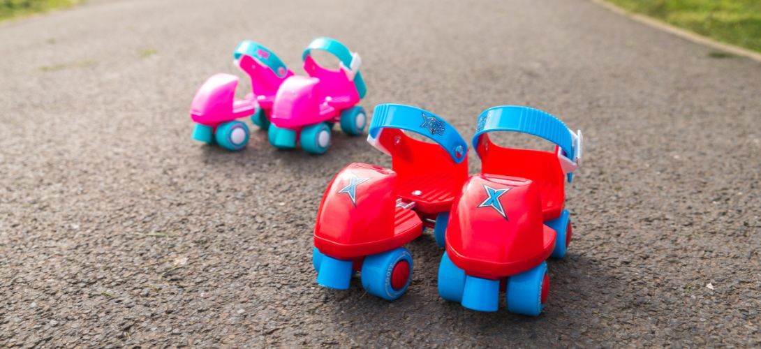 An image of two pairs of pink and red infant skates on a tarmac pavement