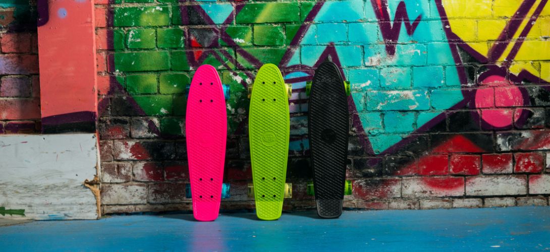 A photo of neon pink, green and black cruiser skateboards against a bright graffiti background